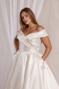 Close-up of a model wearing a plus size lace wedding dress with an off-the-shoulder neckline.