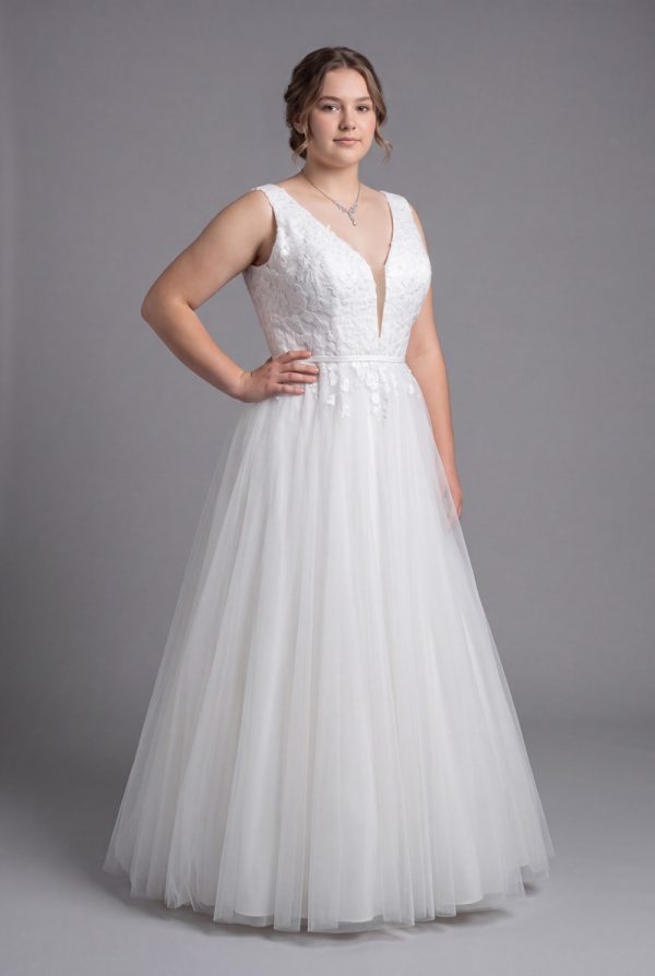 Size 22 model wearing a white plus size deb dress with a V-neck lace bodice and full tulle skirt