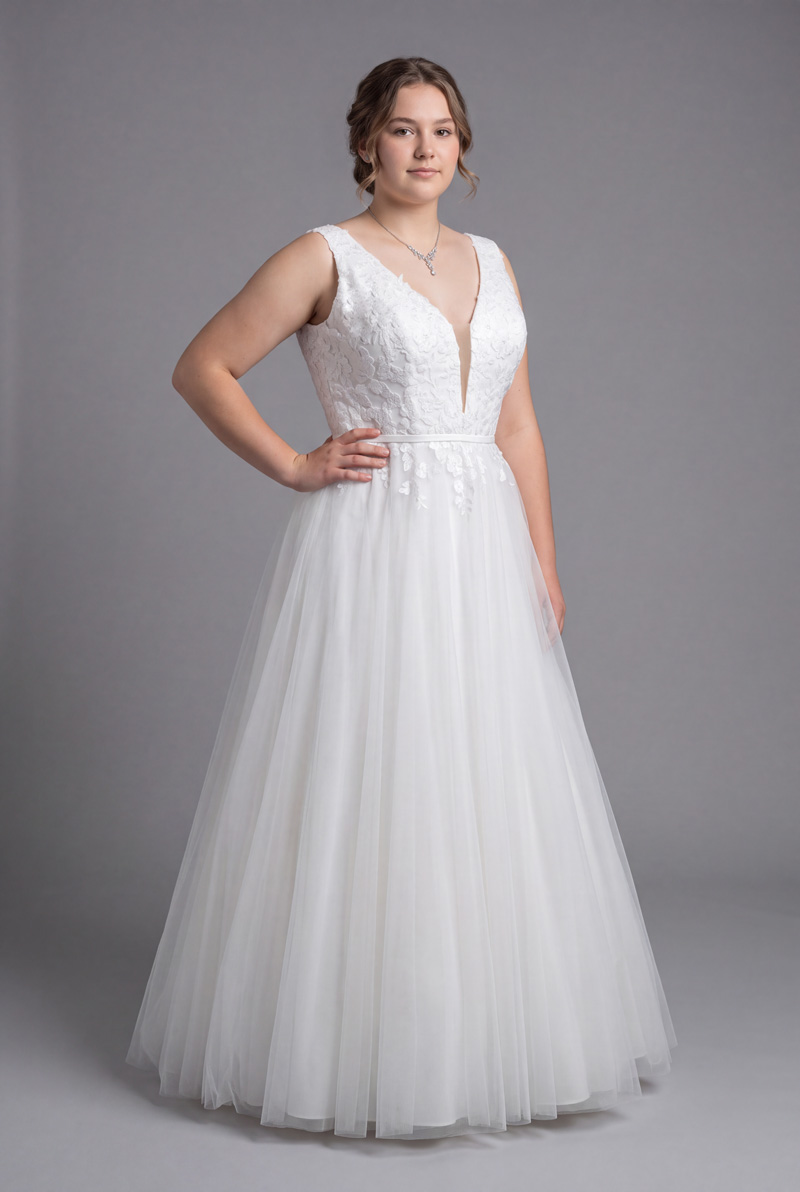 Size 22 model wearing a white plus size deb dress with a V-neck lace bodice and full tulle skirt